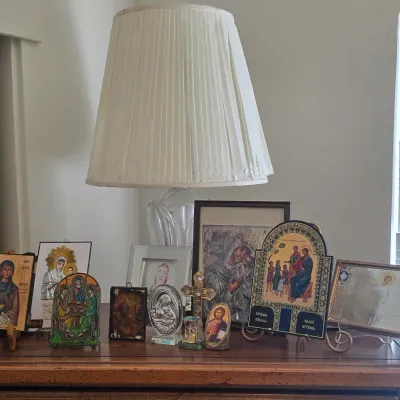 Sale Photo Thumbnail #125: Collection of Christian and Eastern Orthodox religious icons, plaques, and framed artwork displayed on a wooden surface below a table lamp.