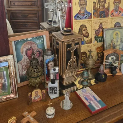 Sale Photo Thumbnail #121: Collection of Orthodox Christian religious art and decor, including painted icons, incense burners, a crucifix, and framed religious images displayed on a wooden surface.
