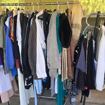 Sale Photo Thumbnail #141: Two rolling clothing racks filled with a large selection of men's and women's vintage and contemporary apparel, including jackets, sweaters, dresses, and button-down shirts.