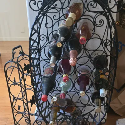 Sale Photo Thumbnail #81: Ornate wrought iron freestanding wine rack with scrollwork details, holding an assortment of bottled beverages.
