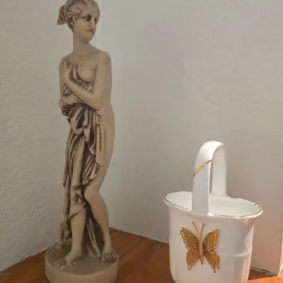 Sale Photo Thumbnail #82: Classical-style resin female figure statue standing beside a white porcelain mini basket featuring a raised gold butterfly accent.