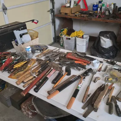 Sale Photo Thumbnail #14: Large assortment of hand tools arranged on a folding table, including hammers, wrenches, loppers, screwdrivers, and a metal toolbox.