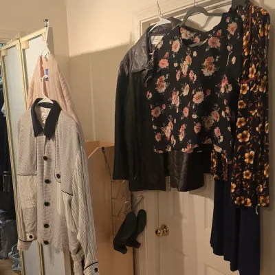 Sale Photo Thumbnail #53: Collection of women's vintage and contemporary clothing, including a leather jacket, floral tops, and patterned button-down shirts hanging on hangers.