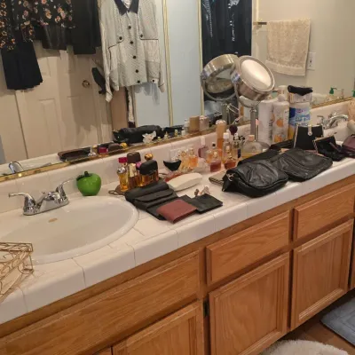 Sale Photo Thumbnail #58: Bathroom vanity lined with assorted items for sale, including vintage perfume bottles, leather purses, wallets, and vanity accessories.