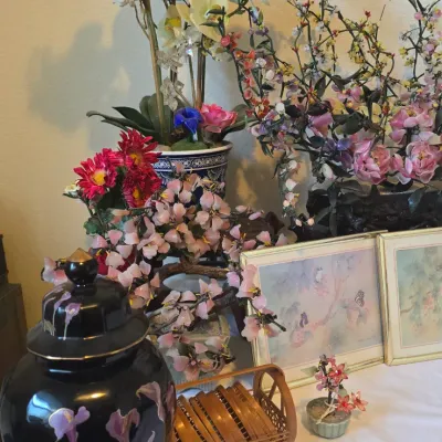 Sale Photo Thumbnail #8: Collection of Asian-inspired home decor including a black porcelain ginger jar with floral motifs, glass flower bonsai trees, artificial orchids, small framed artwork, and a woven wooden coaster set.