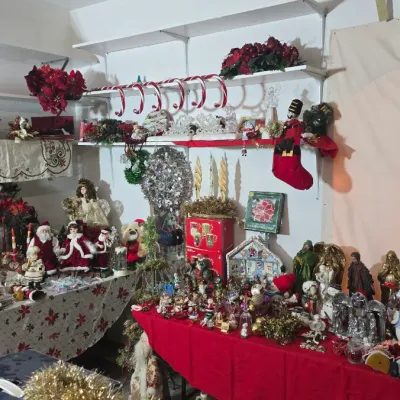 Sale Photo Thumbnail #42: Large assortment of vintage and modern Christmas decorations, including porcelain dolls, Santa figures, tabletop nativity pieces, stockings, and artificial greenery displayed on tables and shelves.