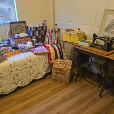Sale Photo Thumbnail #79: Vintage Singer treadle sewing machine in a wooden cabinet, accompanied by an assortment of crafting supplies, baskets, yarn, and framed artwork.
