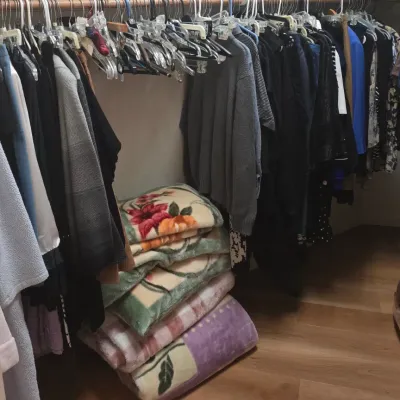 Sale Photo Thumbnail #54: Closet full of women's clothing on hangers, featuring sweaters, jackets, and tops, alongside a stack of plush floral blankets on the floor.