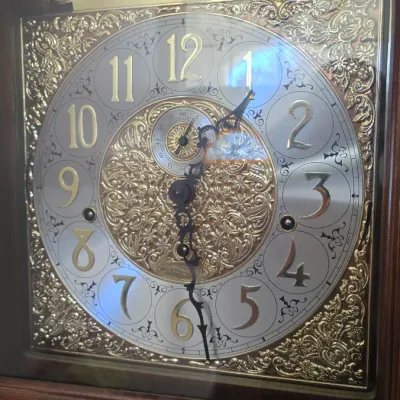 Sale Photo Thumbnail #115: Howard Miller 72nd Edition Anniversary grandfather clock featuring an ornate brass and silver-toned dial with a moon phase dial.