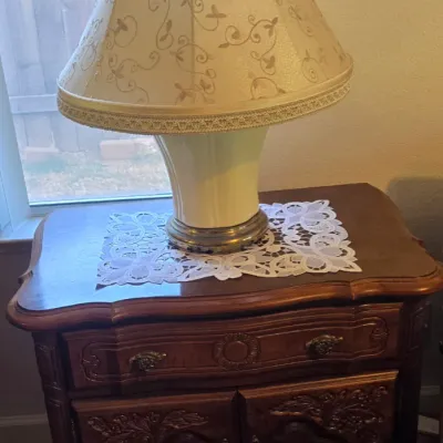 Sale Photo Thumbnail #67: French Provincial style carved wooden nightstand featuring a single drawer over double doors, paired with a ceramic table lamp with a scrolled patterned shade.