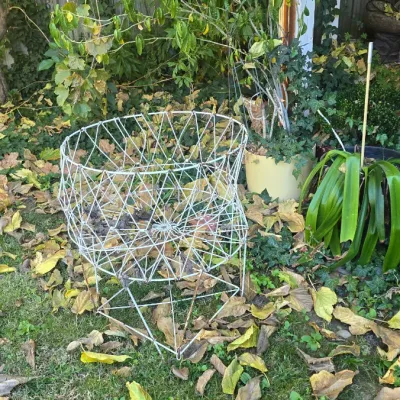Sale Photo Thumbnail #127: Vintage white geometric wire patio chair sitting outdoors in a yard surrounded by fallen leaves.
