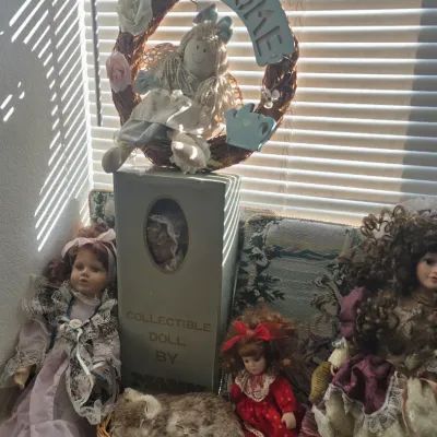 Sale Photo Thumbnail #106: Collection of vintage porcelain dolls, a boxed collectible doll by Mann, a plush cat basket, and a decorative welcome wreath.