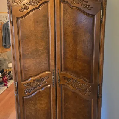 Sale Photo Thumbnail #2: French Provincial style carved wooden armoire featuring an arched crown, floral carvings, and rich wood grain panels.