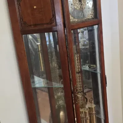 Sale Photo Thumbnail #112: Traditional mahogany grandfather clock with a swan-neck pediment, brass-ornamented dial face, glass display side shelves, and exposed brass weights and pendulum.