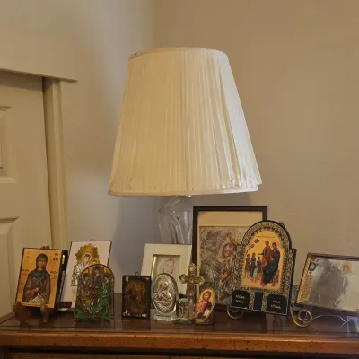 Sale Photo Thumbnail #142: Collection of Christian religious icons, framed images, and small crucifixes displayed on a wooden dresser alongside a crystal table lamp with a pleated shade.
