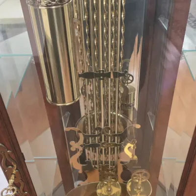 Sale Photo Thumbnail #113: Interior detail of a traditional grandfather clock featuring polished brass weights and an ornate decorative pendulum, enclosed in a wooden display cabinet.