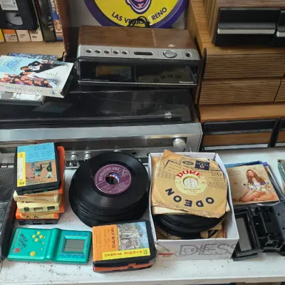 Sale Photo Thumbnail #15: Collection of vintage media and electronics, including 45 RPM records, 8-track tapes, compact discs, cassette players, and a silver stereo receiver.