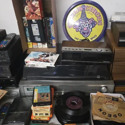 Sale Photo Thumbnail #61: Collection of vintage home audio and video equipment, including VCR players, a Panasonic alarm clock radio, 45 RPM vinyl records, and a Circus Circus Las Vegas wall sign.