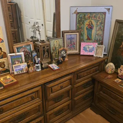 Sale Photo Thumbnail #143: Collection of Christian religious artwork, framed prints, and icons displayed atop a vintage wooden dresser and matching nightstand.