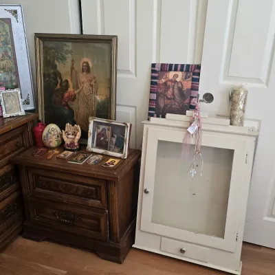 Sale Photo Thumbnail #124: Collection of religious items featuring framed Jesus portraits, icons, figurines, and a white wall-mounted display cabinet sitting on the floor.
