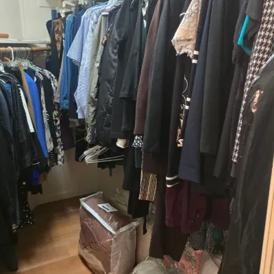 Sale Photo Thumbnail #55: Walk-in closet filled with assorted men's and women's clothing, jackets, shirts, and packaged linens on the floor.