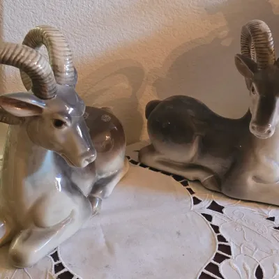 Sale Photo Thumbnail #44: Pair of vintage glazed porcelain ram figurines in shades of grey and beige, depicted in reclining poses.
