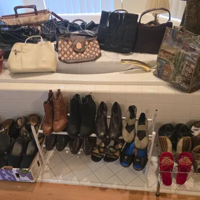 Sale Photo Thumbnail #60: Collection of women's shoes and handbags displayed on a bathtub ledge and floor shoe racks, including ankle boots, sandals, tapestry totes, and leather purses.
