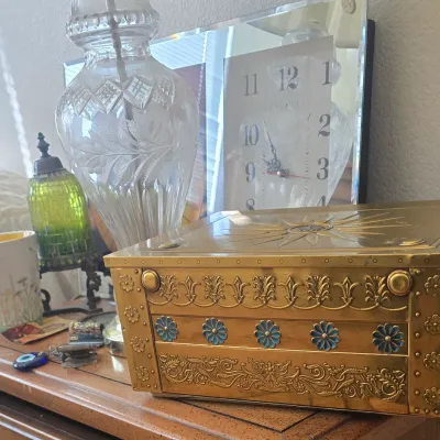Sale Photo Thumbnail #117: Vintage ornate gold-tone metal jewelry box with blue enamel flower accents displayed on a tabletop alongside a cut crystal lamp and ceramic mug.