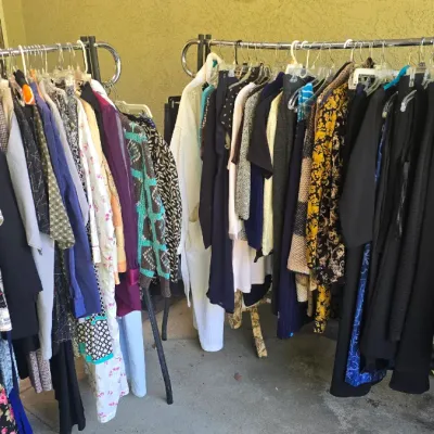 Sale Photo Thumbnail #139: Two metal rolling garment racks filled with an assortment of women's vintage and modern clothing, including dresses, blouses, jackets, and trousers.