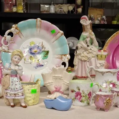 Collection of vintage porcelain and pottery items, including decorative plates, figurines, floral cups, and a ceramic shoe.