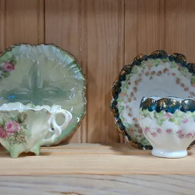 Two antique porcelain teacup and saucer sets featuring floral motifs, ornate scalloped rims, and gilded accents.