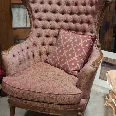 French Provincial style tufted high-back wing chair in mauve damask upholstery, featuring carved wood trim and a matching throw pillow.