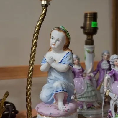 Vintage hand-painted porcelain table lamp featuring a kneeling child figurine in a blue gown on a metal base, displayed alongside other...