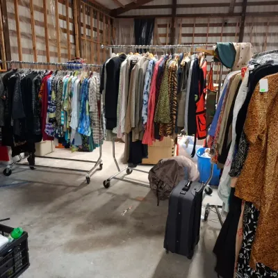 Selection of vintage men's and women's clothing hanging on rolling metal racks in a workshop setting.