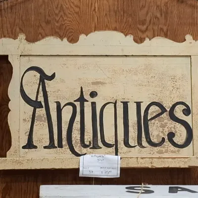 Vintage painted wooden "Antiques" sign crafted from a headboard frame, featuring hand-painted lettering and turned side spindles.