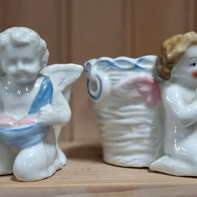 Pair of vintage glazed porcelain cherub figurines featuring blue and pink painted accents, including one figure holding a harp next to a...