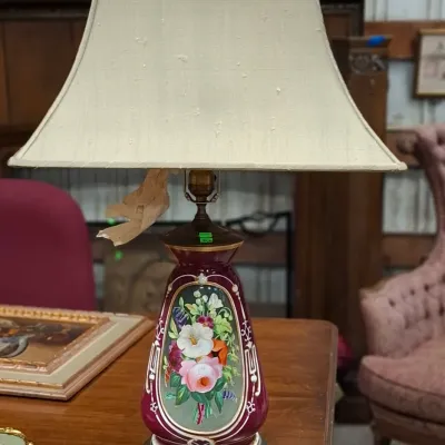 Vintage painted ceramic table lamp with floral medallion detailing, a deep red glaze, and a brass-tone metal base, paired with a beige...