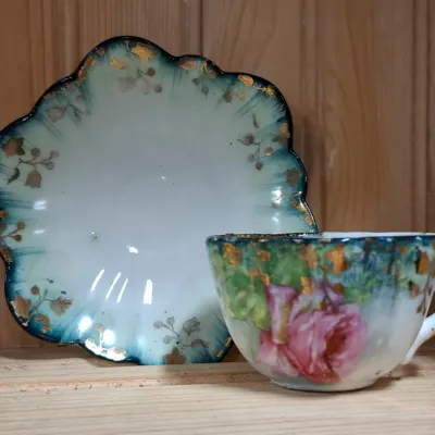 Antique hand-painted porcelain teacup and saucer set featuring a pink rose, teal brushed border, and gilded floral accents with a...