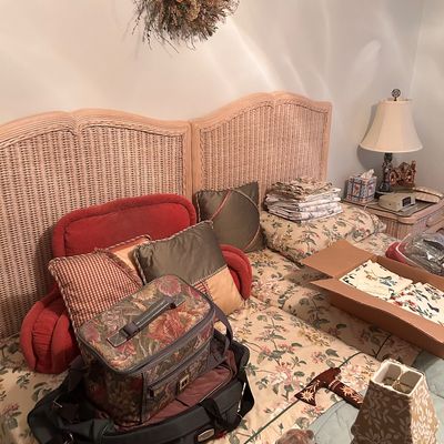 Sale Photo Thumbnail #104: Light wood and wicker twin headboards accompanied by floral bedding, throw pillows, tapestry luggage, linens, and home decor items.