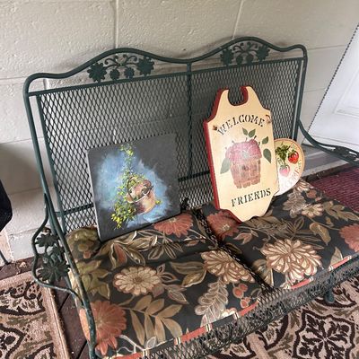 Sale Photo Thumbnail #139: Green wrought iron patio set bench with floral seat cushions, paired with country-style wooden decorative signs and artwork.