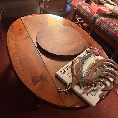 Sale Photo Thumbnail #36: Rustic wooden oval coffee table with a circular wooden insert, a metal rooster wall decor piece, and a oversized Currier & Ives book.