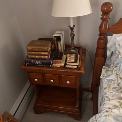 Sale Photo Thumbnail #82: Traditional wooden nightstand with white drawer knobs, paired with a metal candlestick-style table lamp with a cream shade.