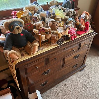 Sale Photo Thumbnail #96: Collection of plush teddy bears in various outfits alongside a vintage wooden chest of drawers.