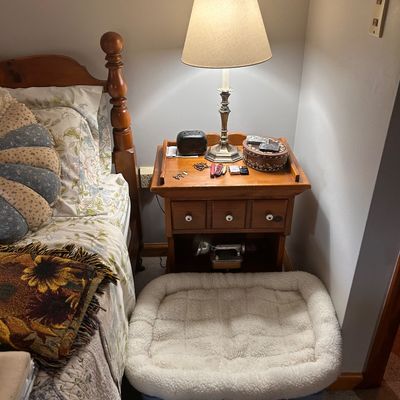 Sale Photo Thumbnail #89: Traditional wooden nightstand with small drawers, topped with a brass table lamp and decorative accessories.