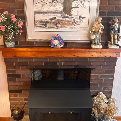 Sale Photo Thumbnail #129: Framed winter bird art print, decorative figurines, and a black metal fireplace stove insert with brick surround.