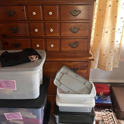 Sale Photo Thumbnail #76: Traditional wooden chest of drawers featuring brass handles and white round knobs alongside plastic storage tubs.