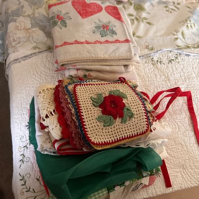 Sale Photo Thumbnail #78: Collection of vintage linens, hand-crocheted potholders with floral motifs, and printed holiday textiles.