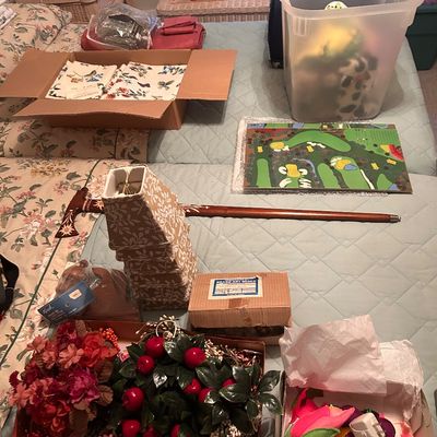 Sale Photo Thumbnail #113: Assorted household items including artificial floral arrangements, boxed textiles, small lamp shades, a carved wooden walking cane, and a golf-themed board game.