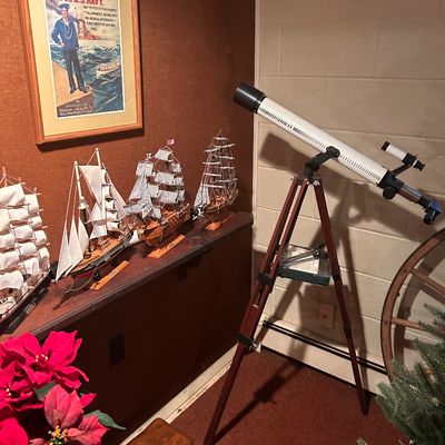 Sale Photo Thumbnail #50: Bushnell refractor telescope on a wooden tripod, shown alongside detailed model sailing ships and a framed US Navy recruitment poster.
