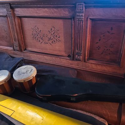 Sale Photo Thumbnail #72: Vintage bongo drums inscribed with "Rat Fink!" alongside instrument cases and a model airplane wing in front of an antique carved wooden bench.